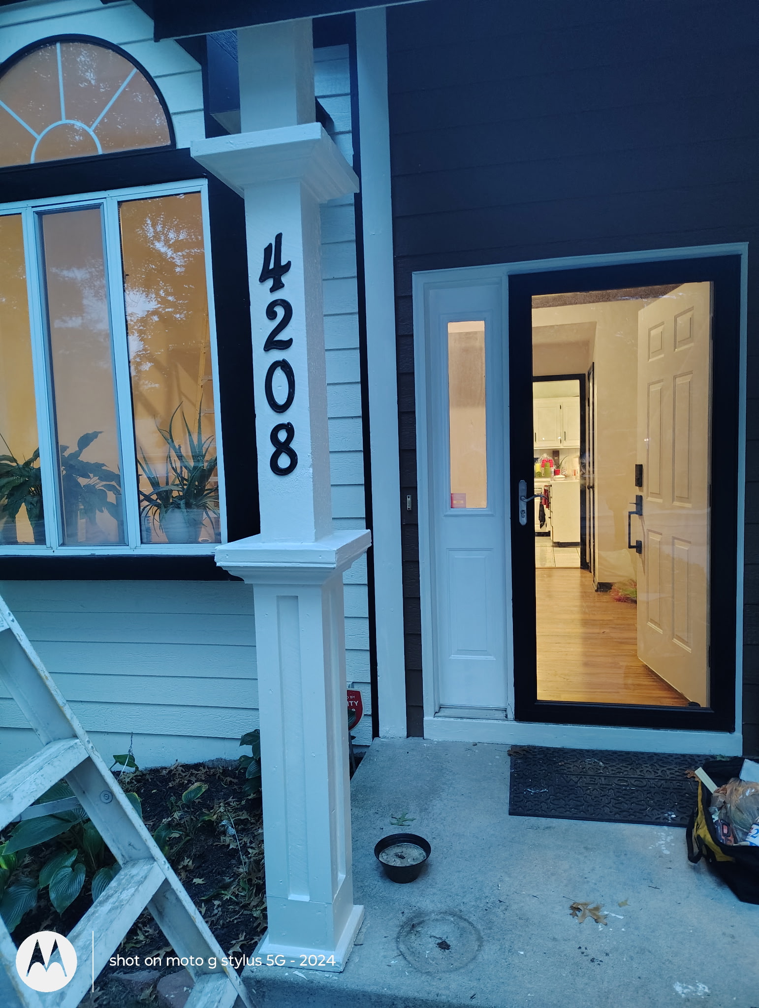 Freshly painted front porch with white trim, black entry door, and house number column
